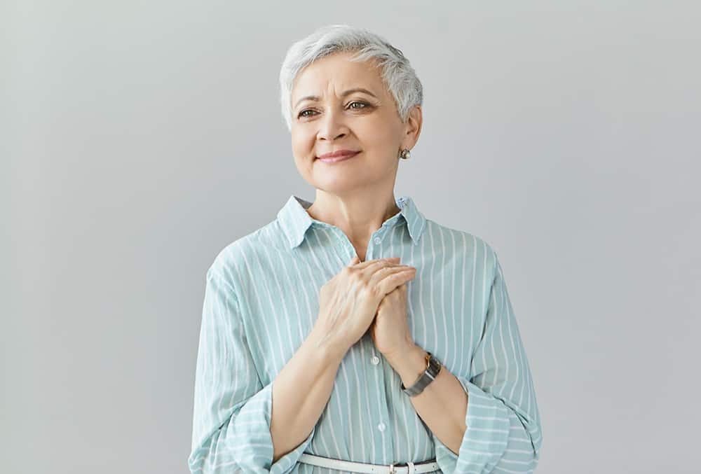 attractive joyful female her sixties posing isolated being touched by heart piercing story movie looking with pleased happy smile holding hands clasped chest kindness gratefulness