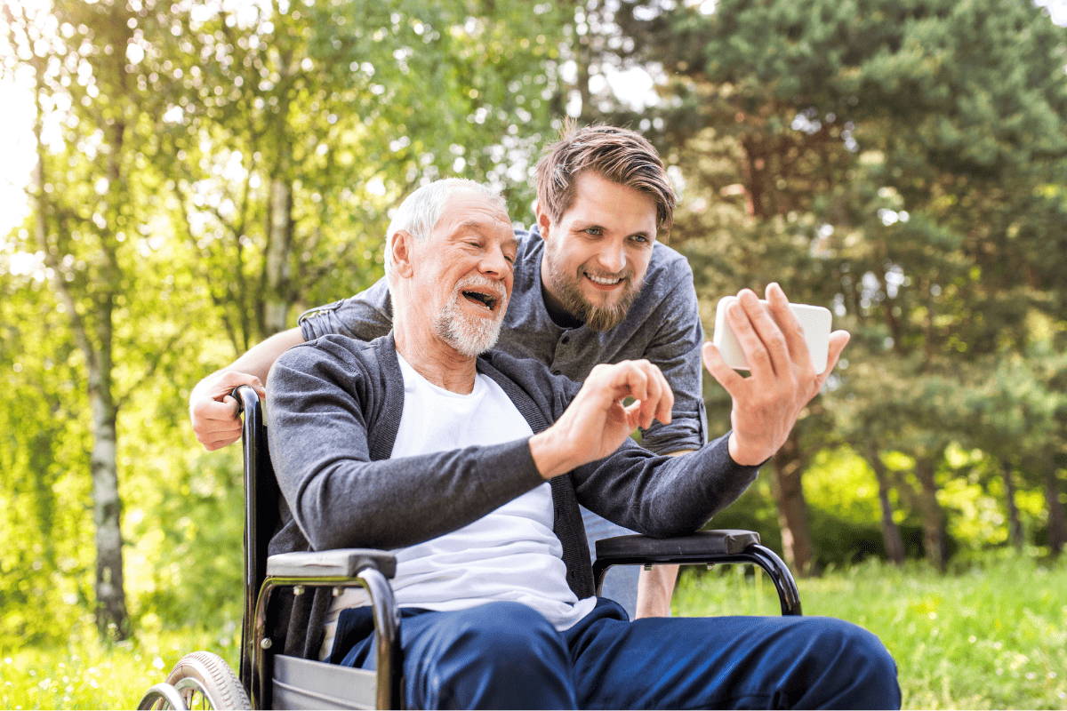 Senior citizen in wheel chair taking selfie outside with younger relative